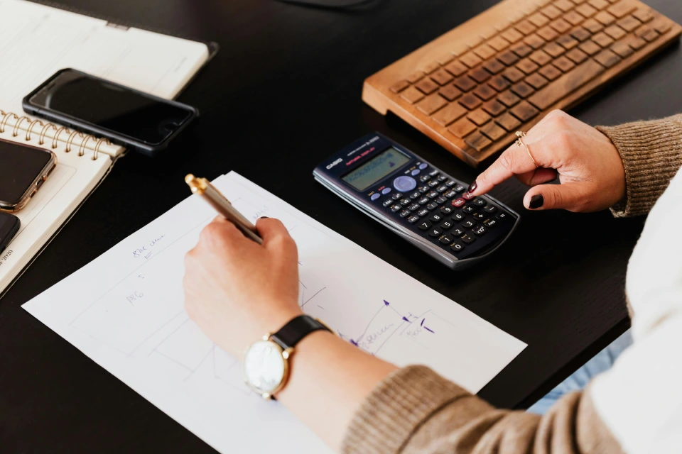 Person calculating finances with pen and calculator.